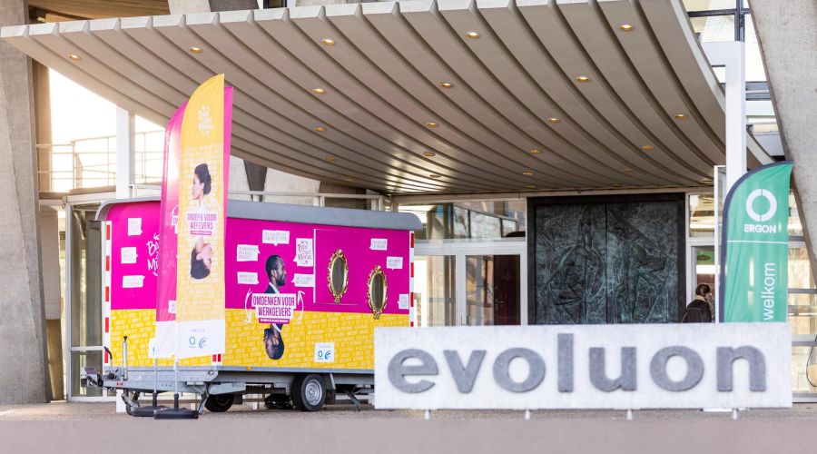 Banners en posters bij de ingang van een gebouw voor de campagne van Ergon en UWV.