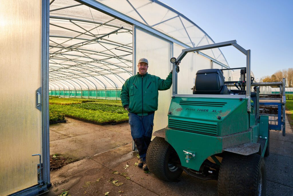 Ergon Kwekerij-medewerker leunt met zijn arm tegen een heftruck aan die voor de planttunnels stilstaat.