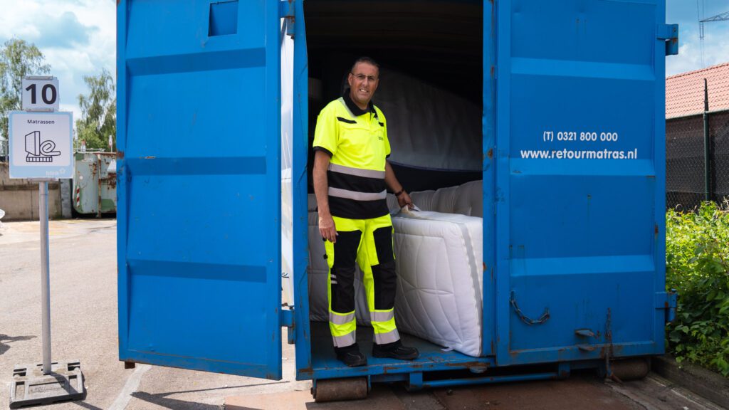 Een medewerker van de milieustraat sleept een matras uit de deuropening van een zeecontainer.
