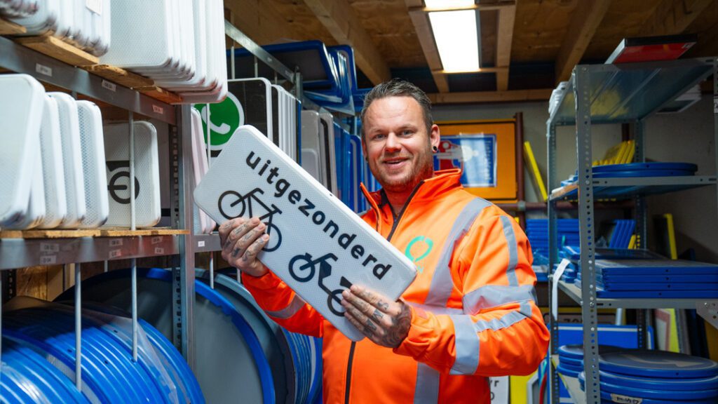 Medewerker pakt verkeerbord voor een fietspad uit een voorraadrek in het magazijn.