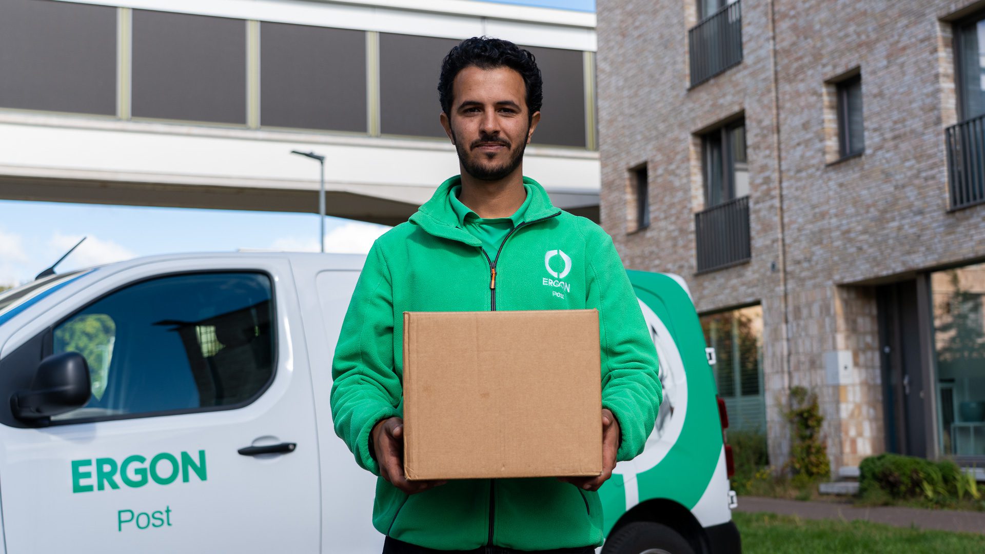 Een medewerker van Ergon Post poseert met een pakket voor een bedrijfswagen.