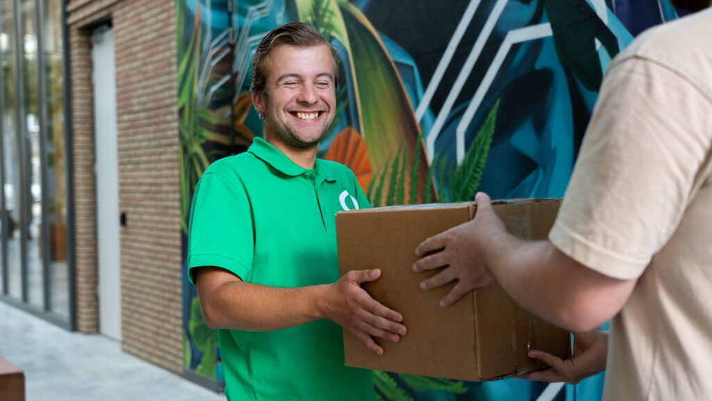 Een medewerker van Ergon Post overhandigt een pakket aan een persoon in een hal.