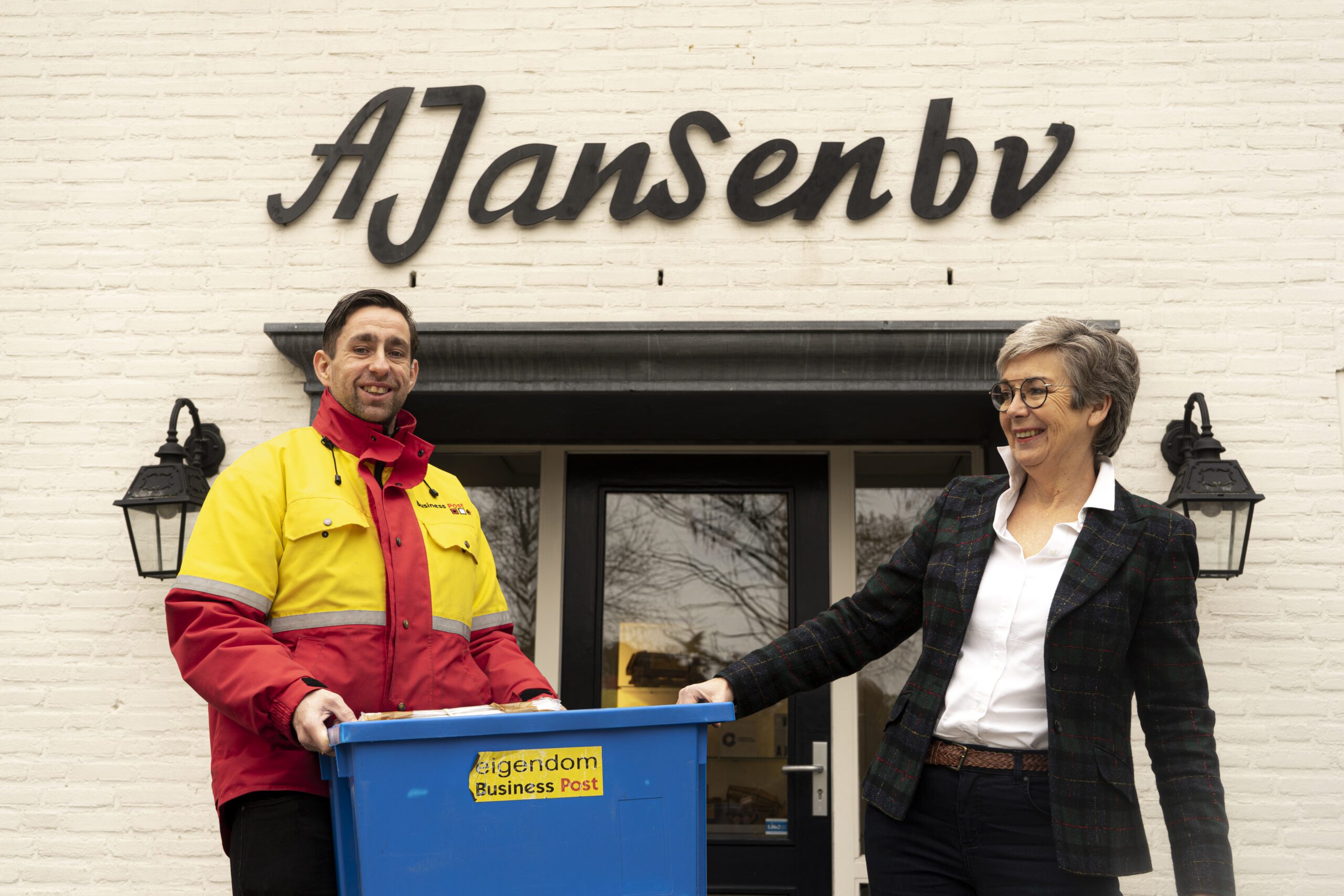 Een medewerker van Ergon Post ontvangt een bak vol post van een vertegenwoordiger van A. Jansen B.V.