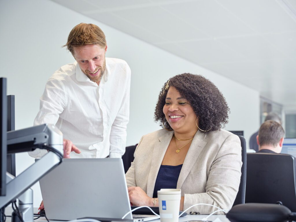 Een leidinggevende legt iets uit aan een gedetacheerde kantoormedewerker terwijl hij naar het scherm wijst.