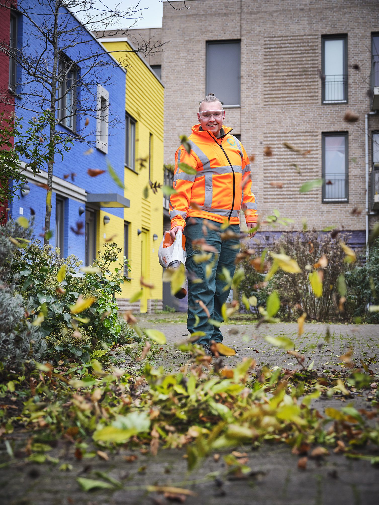 Een medewerker van Ergon Groen blaast herfstbladeren de lucht in met een bladblazer.