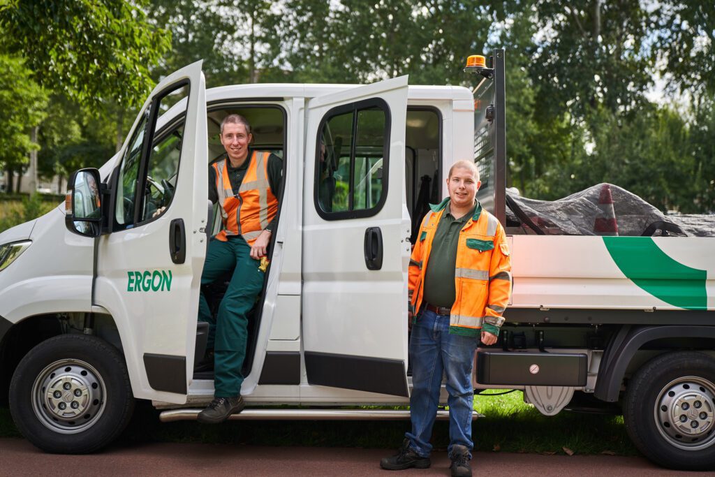 Twee medewerkers staan naast hun werkbus tijdens een pauze.