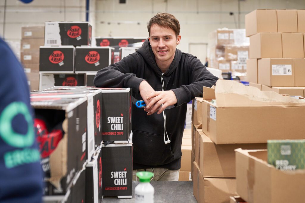 Een medewerker van Ergon Productie staat met een stanleymes in zijn handen tussen twee stapels met dozen.