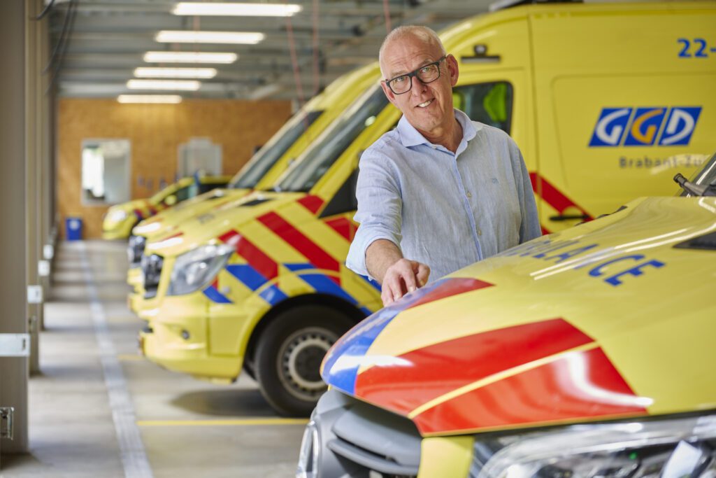 Een vertegenwoordiger van GGD poseert bij geparkeerde ambulances in een garage.