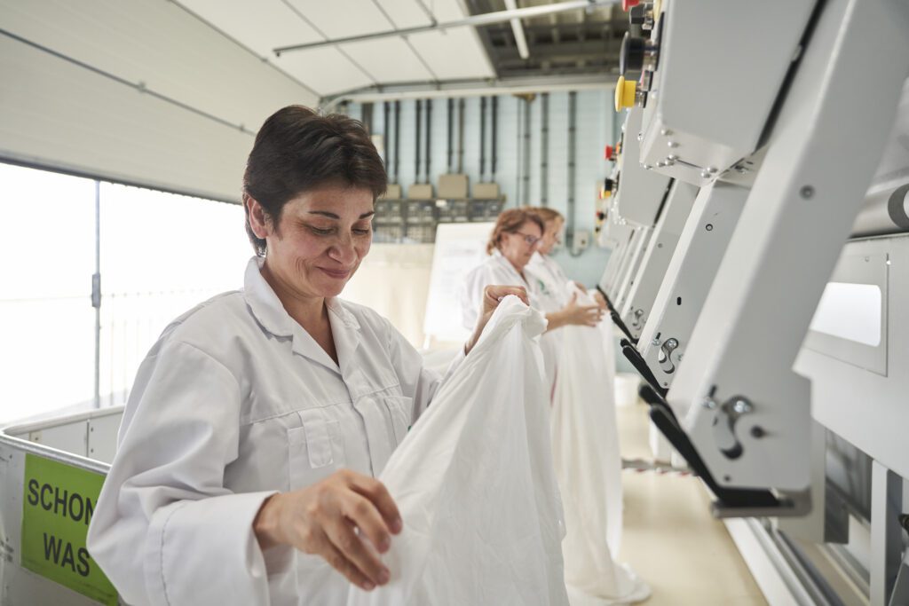 Een medewerker van Ergon Wasserij legt een laken neer op een machine.