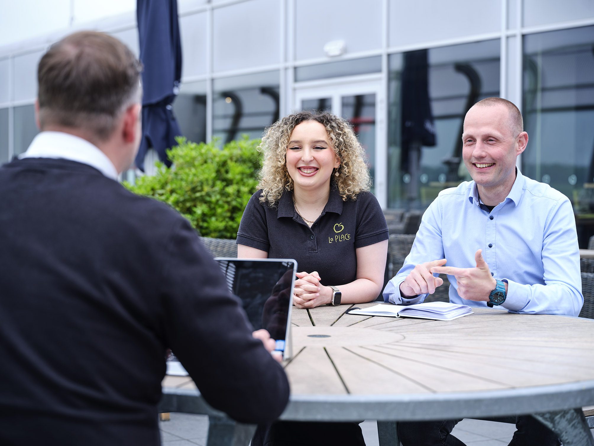 Een driegesprek tussen werkgever, werknemer en de consulent van Ergon aan tafel op een dakterras.
