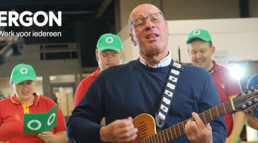 Een medewerker van Ergon speelt gitaar en medewerkers op de achtergrond zingen het Ergon-lied.