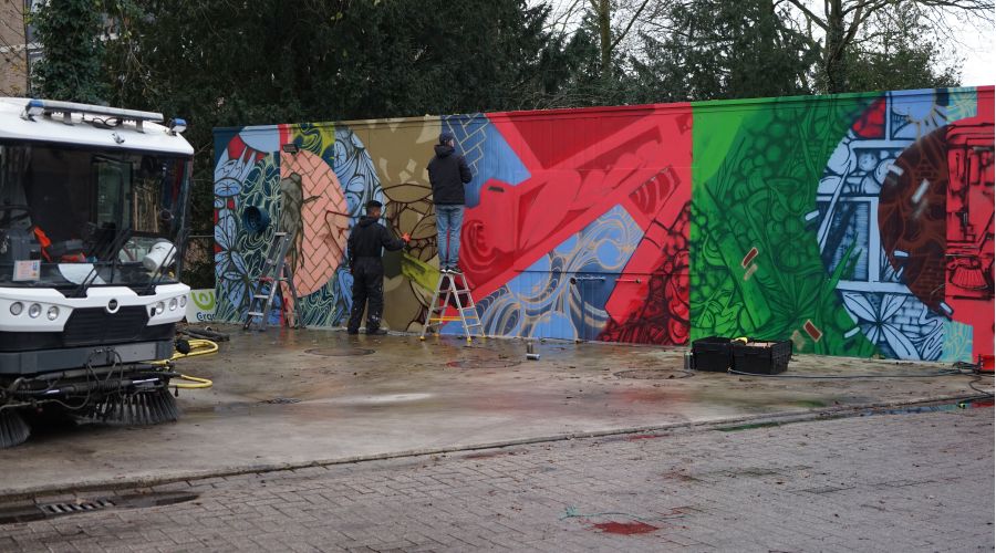 Kunstenaars werken aan een graffiti piece op een keet van Ergon Groen.