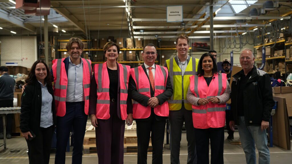 Minister poseert met directieleden en medewerkers in het magazijn